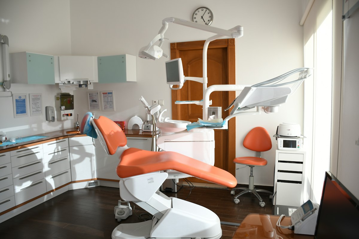 Modern ve aydınlık bir diş kliniğinde, diş cilası uygulamaları için hazır turuncu tedavi koltuğu.