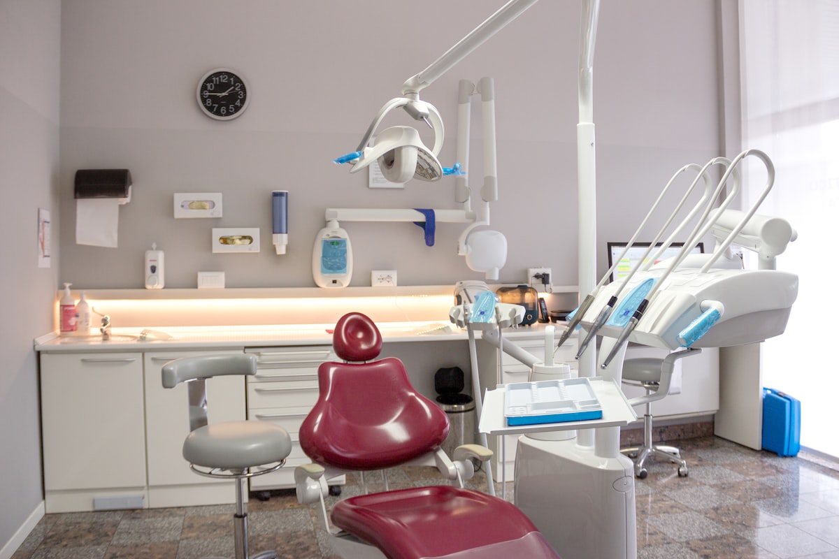 Modern diş kliniği muayene odası, kırmızı koltuk ve lavabo ile hasta konforunu yansıtıyor.